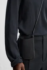 Bolso bandolera negro de cuero con bolsillo plano frontal y correa larga del mismo material.