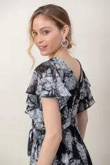 Vestido midi de gasa estampada con flores en tonos negro, gris y blanco, con destellos de hilos de plata. Presenta escote cruzado en V, mangas cortas acampanadas, lazo ajustable en la cintura y falda de corte asimétrico.