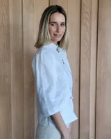 Camisa de manga tres cuartos color beige con cuello con volados y botones frontales. Presenta un detalle de color negro en la parte superior de las mangas.