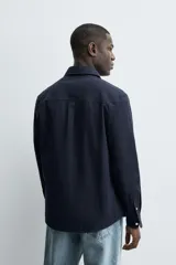 Camisa de corte regular fit confeccionada en tejido de algodón con textura. Presenta cuello solapa, cierre frontal de botones, manga larga con puños abotonados y un bolsillo plastrón en el pecho.