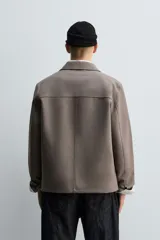 Sobrecamisa de corte relajado confeccionada en tejido compacto con lana. Presenta cuello solapa, cierre frontal con botones, mangas largas con puños abotonados y dos bolsillos de plastrón en la parte frontal.