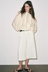 Chaqueta bomber de cuello subido y manga larga, con acabado satinado en color beige. Presenta pliegues frontales, bolsillos laterales ocultos en costura y cierres elásticos en puños y cintura. Cierre frontal con cremallera.