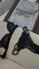 Conjunto de lencería negro de encaje, compuesto por un soutien triangular con breteles finos y una tanga con tiras cruzadas.