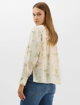 Blusa de algodón con estampado floral de flores silvestres sobre fondo claro. Presenta cuello redondo con detalle de puntilla, abotonadura frontal, canesú con frunces y mangas largas con puños elásticos decorados con puntilla.