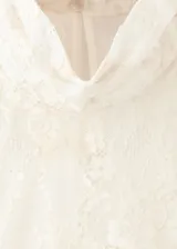 Blusa de encaje color crema con cuello alto, mangas largas con volados en los puños y detalle de volado en el ruedo.