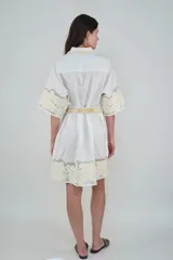 Vestido corto de lino blanco con cuello clásico, mangas cortas y detalles bordados florales tono sobre tono con inserciones translúcidas. Incluye un cinturón de tela ajustable con estampado.