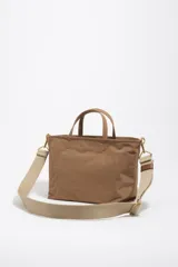 Bolso shopper mediano de mano Bimba y Lola color marrón, confeccionado en poliamida con detalles en cuero y herrajes metálicos dorados. Cuenta con doble asa de mano, correa de hombro ajustable de lona beige, cierre superior con cremallera y logo impreso en dorado al frente.