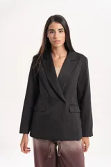 Blazer de corte sastrero en color negro, con diseño de doble botonadura frontal y solapas clásicas. Presenta dos bolsillos laterales con solapa y mangas largas.