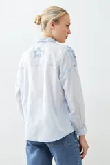 Camisa de corte recto y manga larga en color celeste claro, con diseño de estrellas bordadas en relieve en tono azul. Presenta cuello clásico y cierre frontal con botones.