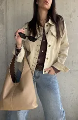 Sobrecamisa beige de gabardina con tachas metálicas decorativas en el cuello y la solapa frontal. Cuenta con bolsillos con solapa en el pecho y cierre frontal con botones.