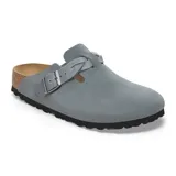 Zueco tipo mule de gamuza color gris, con diseño de tira trenzada sobre el empeine y hebilla metálica ajustable. Cuenta con plantilla de corcho anatómica y suela de goma negra.