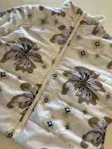 Campera puffer color beige con estampado floral y de logotipos en tonos marrones y grises, cuello alto y cierre frontal con cremallera.