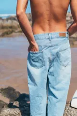 Pantalón de jean corte loose fit color celeste claro, con diseño de cinco bolsillos y estampa vertical con la frase 'GLASSYWAVES' en la pierna derecha.