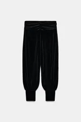 Pantalón negro de tiro bajo, confeccionado en terciopelo con pequeños puntos brillantes. Presenta cintura elástica con pliegues, caída ancha tipo baggy y puños ajustados en los tobillos.
