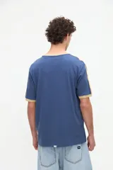 Remera de manga corta azul con cuello redondo, puños y bandas en los hombros en color tostado. Presenta un pequeño bordado rojo en el pecho y está confeccionada en suave jersey de algodón con calce clásico.