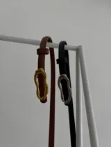 Cinturón fino de ecocuero, con hebilla ovalada irregular metálica.