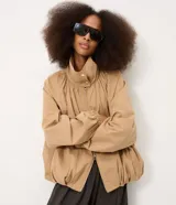 Campera bomber de sarga color beige, con diseño cortavientos, cuello alto con botones a presión y cierre frontal. Presenta mangas largas con puños elastizados, pliegues delanteros que aportan volumen y ruedo con elástico. Marca Renner.