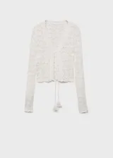 Cardigan de crochet color blanco, con cuello en V, manga larga y cierre frontal mediante lazos con borlas. Presenta un diseño calado con textura.