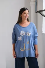 Remera de algodón color celeste, con cuello redondo amplio, mangas largas y estampa frontal de flores en tonos blanco y dorado.