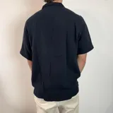 Camisa de hombre color verde oliva, de muselina con textura arrugada, manga corta, corte oversize, cuello cubano y cierre con botones. Presenta un pequeño logo bordado en el pecho.