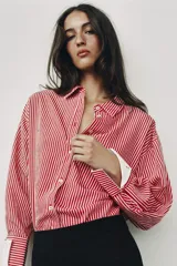 Camisa de cuello solapa y manga larga con rayas verticales rojas y blancas, con puños anchos blancos contrastantes y cierre frontal de botones.