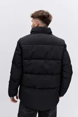 Cazadora acolchada negra con capucha, cierre frontal con cremallera y diseño de paneles horizontales. Presenta un parche decorativo en la manga y un ajuste cómodo.