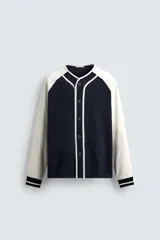 Chaqueta de corte relajado con diseño color block, cuerpo en color azul marino y mangas en color blanco. Presenta cuello redondo, cierre frontal con botones y puños de rib a rayas.