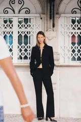 Pantalón negro de tiro alto, corte flare (campana) y pinzas frontales. Presenta bolsillos laterales y falsos bolsillos de vivo en la espalda.