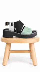 Sandalias de cuero con plataforma y suela track. Presentan diseño multicolor que combina tiras anchas en color negro, una tira delantera en cuero texturizado verde menta con acabado tipo cocodrilo y detalles en plateado metalizado en el talón. Cuentan con tira ajustable con hebilla en el tobillo.