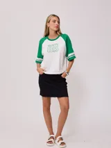 Remera bicolor Rusty de corte holgado y estilo deportivo, con cuerpo blanco y mangas raglán azules con doble raya blanca. Presenta estampado frontal con el texto 'RUSTY 85'.