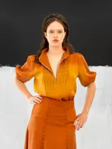 Blusa color ocre de algodón tipo seda, teñida a mano con técnica tie dye. Tiene corte recto, cierre invisible en el escote delantero y mangas regulables con elástico.