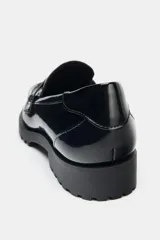 Mocasín de estilo penny en material sintético con acabado acharolado brillante. Presenta un diseño de punta redonda, antifaz clásico en el empeine y una suela dentada robusta.