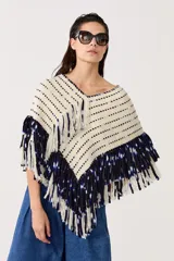Poncho tejido plano de lana merino color natural con flecos bordados a mano en azul marino. Tiene escote en V y largo a la cadera.