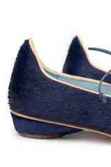 Zapato tipo blucher de pelo pony en color azul marino, con cierre de cordones y ribetes en color ocre. Presenta una silueta geométrica con aberturas laterales y tacón forrado en forma de lágrima.