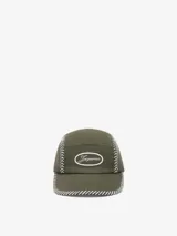 Gorra de 5 paneles color verde oliva, confeccionada en lona de algodón. Presenta costuras de punto de silla de montar en blanco a lo largo de los paneles y el borde de la visera. En el frente tiene un parche ovalado con el logo bordado en blanco.