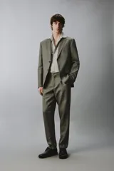Pantalón de traje regular fit de lino color verde militar, con bolsillos laterales y bolsillos traseros de doble vivo con botón. Cierre frontal con cremallera y botón.