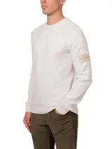 Remera blanca de manga larga con cuello redondo y puños de canalé. Tiene un parche con el logo de Calvin Klein en la manga.