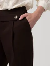 Pantalón de vestir color marrón oscuro, de corte recto y tiro alto. Confeccionado en una mezcla de lana y poliéster reciclado, presenta una pretina limpia con un botón lateral decorativo y cierre invisible lateral.