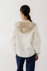 Blusa de lino color beige con cuello de crochet tejido y lazos frontales para anudar. Presenta mangas largas abullonadas con puños ajustados.