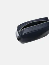 Cartera tipo camera bag de Calvin Klein, color azul marino oscuro, con textura de cuero granulado. Presenta un logo CK grabado en bajo relieve en el frente y una correa ajustable de tela gris claro.