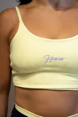 Top deportivo color amarillo claro con textura sutil y logo de la marca en color lila.