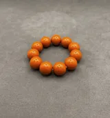 Pulsera elástica compuesta por cuentas esféricas de resina en tonos verde lima, naranja y bordó.