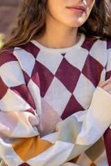 Sweater tejido de algodón con diseño de rombos multicolor en tonos marrones, azul y rojo. Presenta una silueta oversize, cuello redondo y mangas largas abullonadas con puños ajustados.