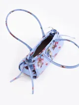 Cartera de hombro de cuero vacuno color celeste con estampado floral multicolor. Cuenta con cierre superior, bolsillo interno, asas largas y detalles de herrajes metálicos con candado y llavero colgante en el frente.