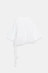 Camiseta de algodón con cuello redondo y manga corta. Presenta un bajo asimétrico confeccionado en un tejido ligero con volantes y una tira lateral decorativa con volantes.