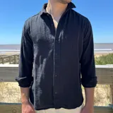 Camisa de lino color negro, con cuello camisero, cierre frontal de botones y mangas largas con puños simples.