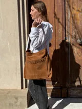 Cartera tipo tote bag de cuero color camel, con detalles de tachas metálicas en el bolsillo frontal y tiras largas para el hombro.