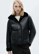 Chaqueta de doble faz con exterior de cuero sintético negro y forro interior de pelo sintético al tono. Presenta cuello camisero, cierre frontal con botones, manga larga y dos bolsillos de parche delanteros.