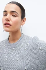 Sweater color beige melange de tejido de punto con diseño de trenzas y detalles de perlas en el frente y las mangas.