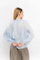 Blusa celeste de algodón con escote en V con lazos y mangas largas abullonadas con puños elásticos.